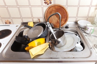 domestic kitchen with dirty crockery and cutlery in messy sink